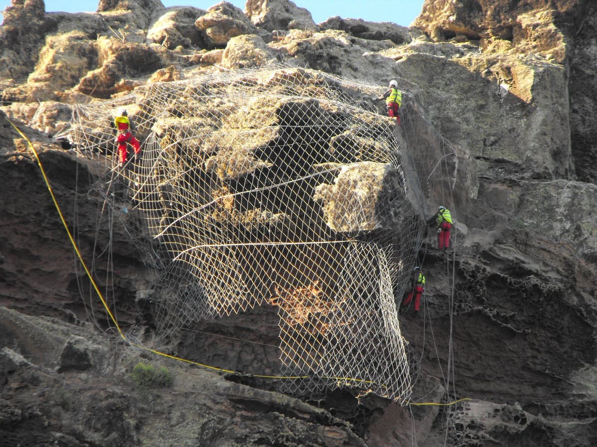 Rope access crew securing steel mesh on a rock mass