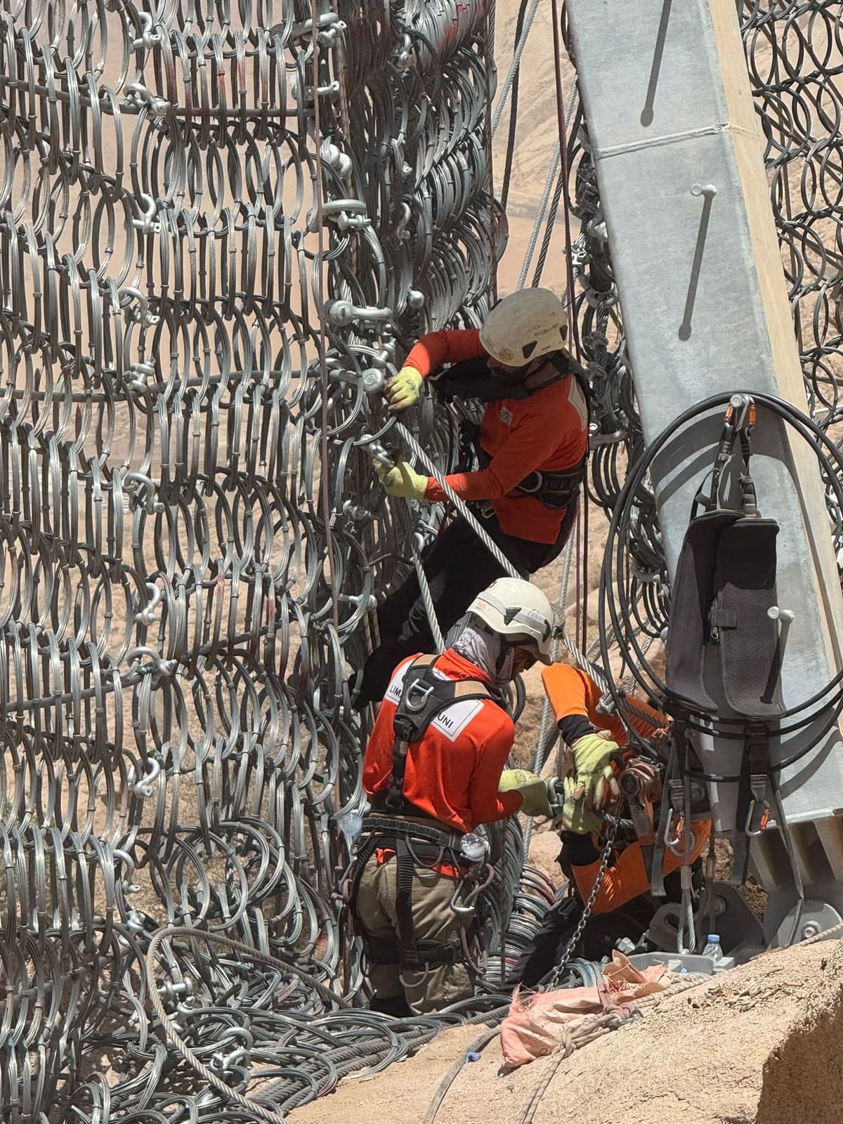 Two technicians installing ring net on a rockfall barrier
