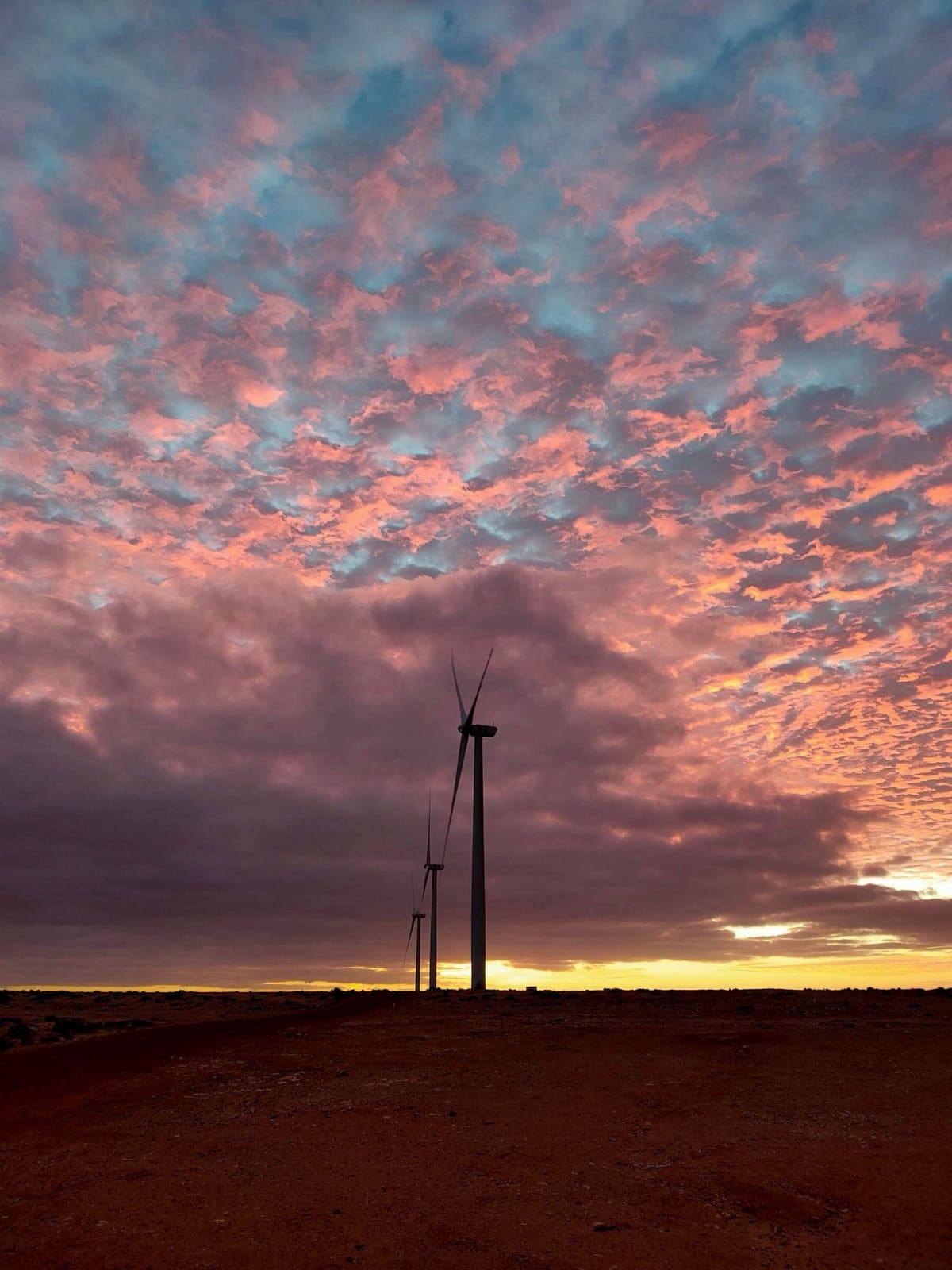 Three wind turbines under a dramatic sunrise sky